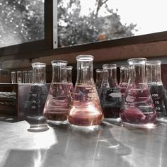 several flasks filled with liquid sitting on top of a metal table next to a window