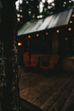 a wooden deck with chairs and lights on the trees in front of a cabin at night