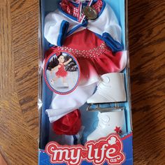 the doll is in its box on the wooden table with it's clothes and accessories