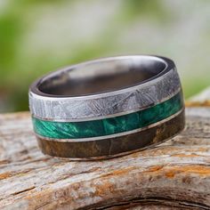 a wedding band with green and silver inlays on top of a piece of wood