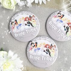 three bride tribe buttons sitting on top of a table next to flowers and white flowers