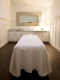 a large white bed sitting in a bedroom next to a bathroom sink and vanity with a mirror above it