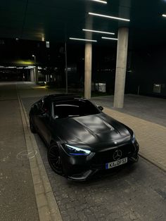 a black sports car parked in front of a parking garage at night with its lights on