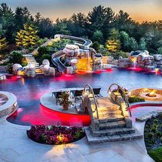 an outdoor swimming pool surrounded by landscaping and water features at sunset or dawn with red lights on the steps