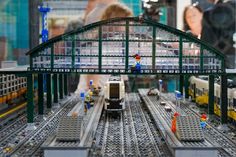 a model train station with trains on tracks and people standing near the platform, all in legos