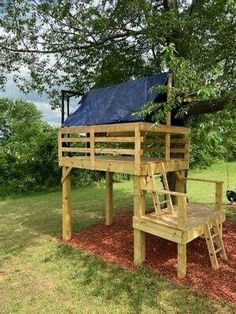 a wooden tree house with a blue tarp on the roof and stairs to it