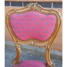 a pink and blue chair sitting on top of a cement floor next to a brick wall