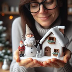 a woman holding a small house with a snowman and santa clause on it