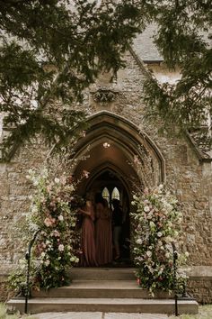 two women in long dresses standing at the entrance to an old building with flowers on it