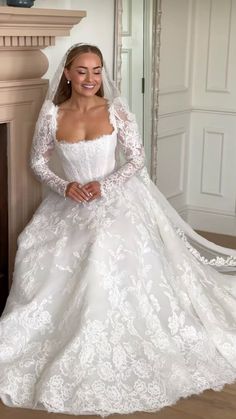 a woman in a white wedding dress standing next to a fireplace with her hands on her hips