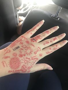 a person's hand with red and white designs painted on it, sitting in a car