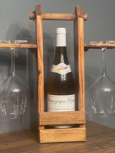 a bottle of wine sitting on top of a wooden shelf next to two empty glasses