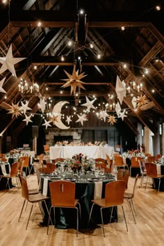 a room filled with lots of tables covered in white and black table cloths, stars hanging from the ceiling