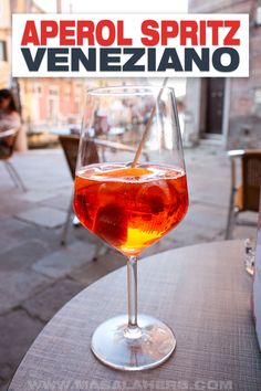 a glass of wine sitting on top of a table next to a sign that says aperol spritz veneziano