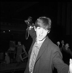 a man in a suit and tie is holding a microphone up to his ear as people watch from behind him