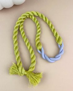 a yellow and blue rope with tassels on it next to a white vase