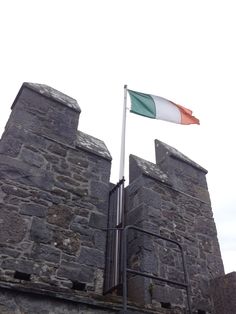 an irish flag flying on top of a stone building with a gate in the foreground