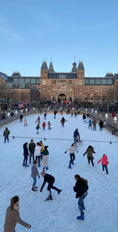 many people are skating on an ice rink in front of a large building with a clock tower