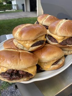 several hamburgers sitting on top of a white plate next to a bbq grill