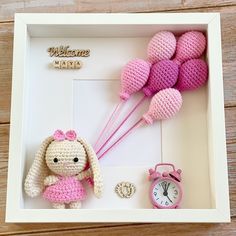 a crocheted doll in a white box with pink balloons and a small clock