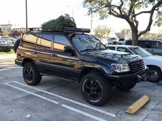 a black suv parked in a parking lot next to other cars and trees on top of it