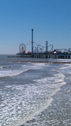 people are walking on the beach near an amusement park