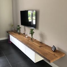 a flat screen tv mounted to the side of a wall next to a wooden shelf