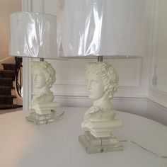 two white marble busturines sitting on top of a table next to a lamp