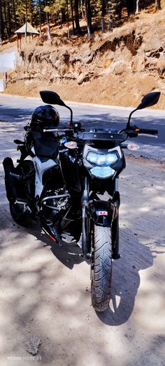 the motorcycle is parked on the side of the road in front of some trees and dirt