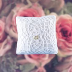 a close up of a ring on a pillow with flowers in the backgroud