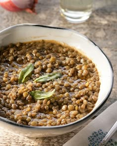 a white bowl filled with green lentils and garnished with basil leaves on top