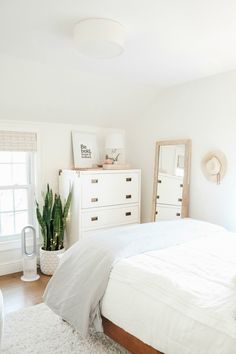 a bedroom with white furniture and plants in the corner