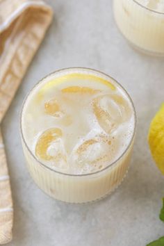 two glasses filled with lemonade and ice on a table next to some lemons