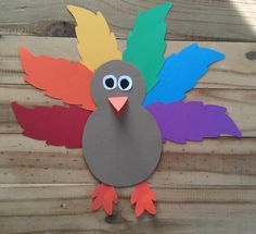 a turkey made out of colored paper sitting on top of a wooden table