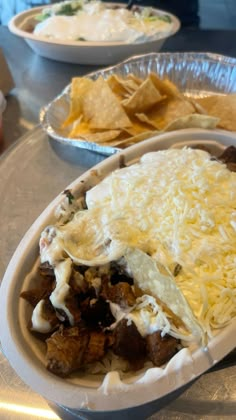 two plates filled with food sitting on top of a table next to bowls of chips