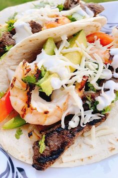 two tacos filled with meat, shrimp and vegetables on top of tortillas