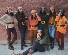 a group of women standing next to each other in front of a wall wearing costumes