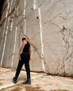 a man walking in front of a large rock wall with white birch trees on it