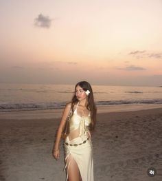 a woman in a white dress walking on the beach at sunset with her hair down