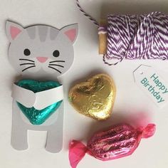 a cat with a heart shaped box next to some candy and twine on a table