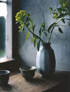 a vase with flowers in it sitting on a table next to a bowl and cup