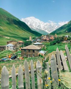 a small village in the mountains surrounded by greenery and wooden fences with snow - capped mountains in the background