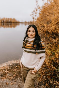 a woman standing in front of a body of water wearing a striped sweater and khaki pants