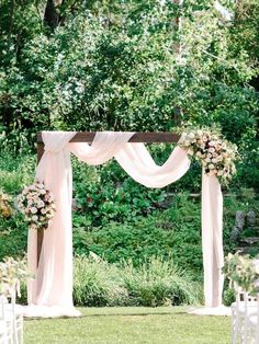 an outdoor ceremony setup with white chairs and pink flowers on the aisle, surrounded by greenery