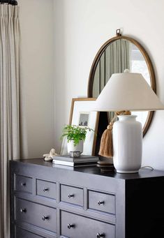 a white vase sitting on top of a black dresser next to a mirror and lamp