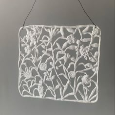 a white wall hanging with flowers and leaves on it's side, in the shape of a rectangle