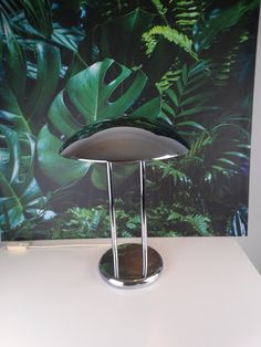 a table lamp sitting on top of a white counter next to a wall with green plants