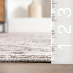 a ruler is on the floor next to a white bed with a gray and beige rug