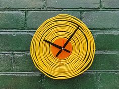 a yellow clock on the side of a brick wall with a black handset in the shape of a hose