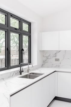 a white kitchen with marble counter tops and black framed windows in the backround